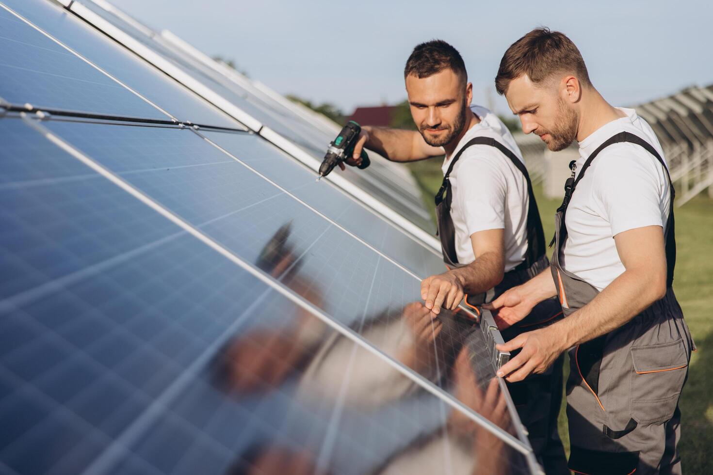 Two skilled workers or craftsmen wearing working gray uniforms, technicians are installing solar panels on a solar farm for clean energy and electricity supply photo