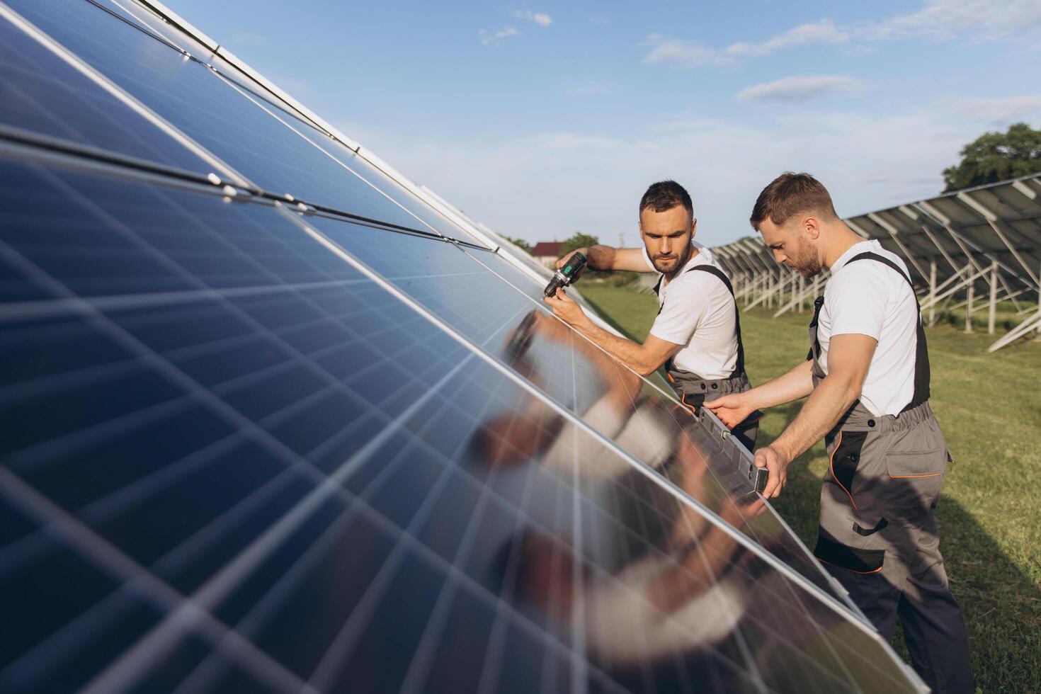 Two skilled workers or craftsmen wearing working gray uniforms, technicians are installing solar panels on a solar farm for clean energy and electricity supply photo