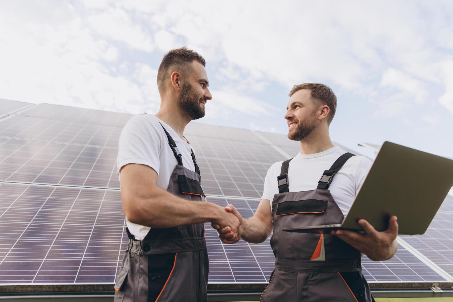 Energy specialist using digital tablet reading information to check the efficiency of solar panel construction. Green energy jobs. Technology. Two solar power plant workers hand shake photo