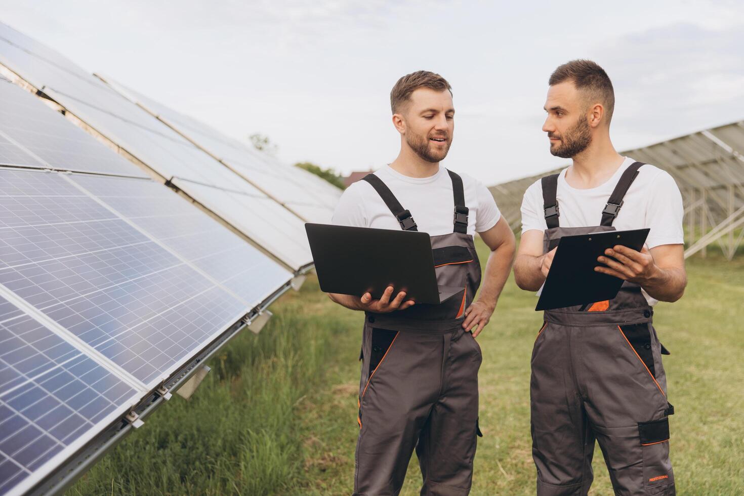 Energy specialist using digital tablet reading information to check the efficiency of solar panel construction. Green energy jobs. Technology. Two solar power plant workers are recording data photo