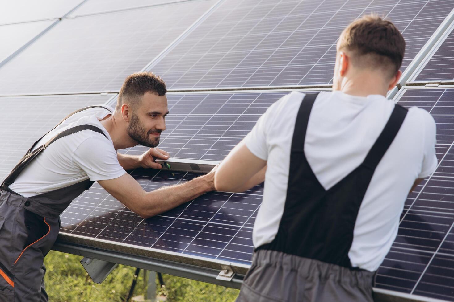 Two skilled workers or craftsmen wearing working gray uniforms, technicians are installing solar panels on a solar farm for clean energy and electricity supply photo
