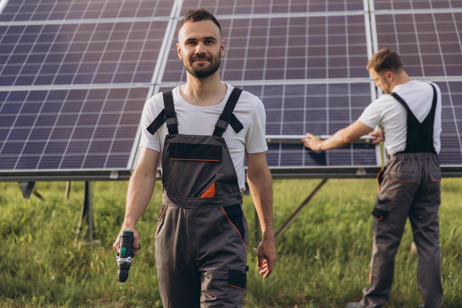 dos experto trabajadores o artesanos vistiendo trabajando gris uniformes, técnicos son instalando solar paneles en un solar granja para limpiar energía y electricidad suministro foto