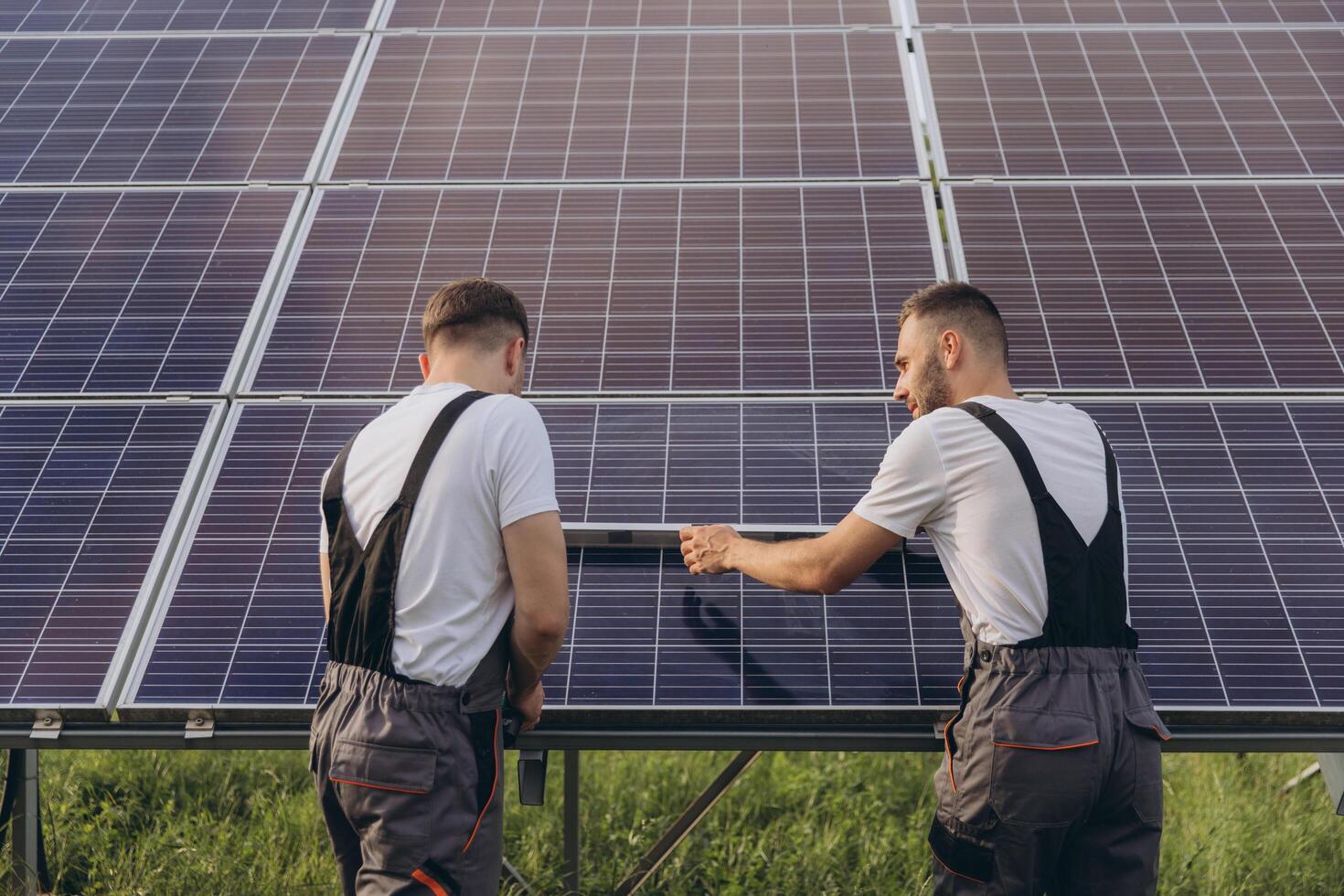 Two skilled workers or craftsmen wearing working gray uniforms, technicians are installing solar panels on a solar farm for clean energy and electricity supply photo