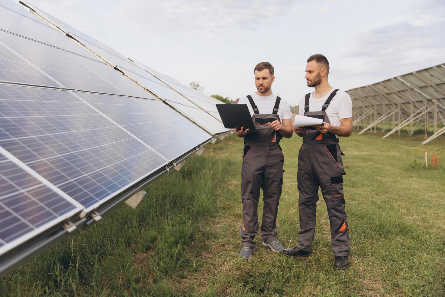 Energy specialist using digital tablet reading information to check the efficiency of solar panel construction. Green energy jobs. Technology. Two solar power plant workers are recording data photo