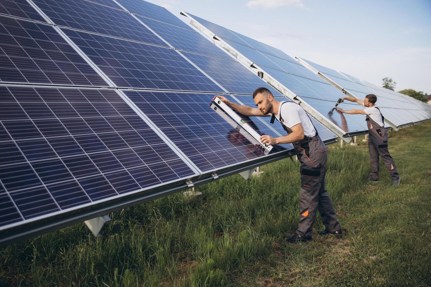 Two skilled workers or craftsmen wearing working gray uniforms, technicians are installing solar panels on a solar farm for clean energy and electricity supply photo
