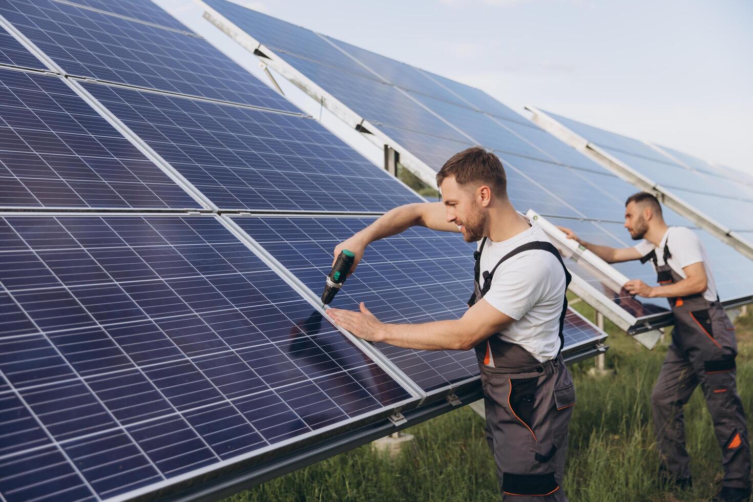 Two skilled workers or craftsmen wearing working gray uniforms, technicians are installing solar panels on a solar farm for clean energy and electricity supply photo