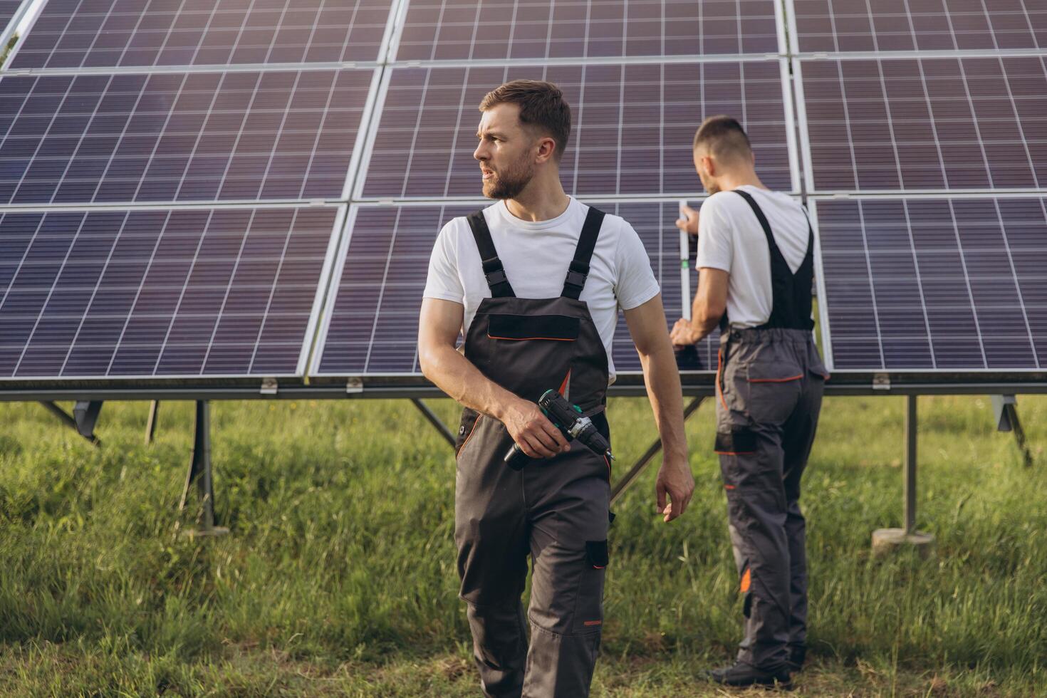 Two skilled workers or craftsmen wearing working gray uniforms, technicians are installing solar panels on a solar farm for clean energy and electricity supply photo