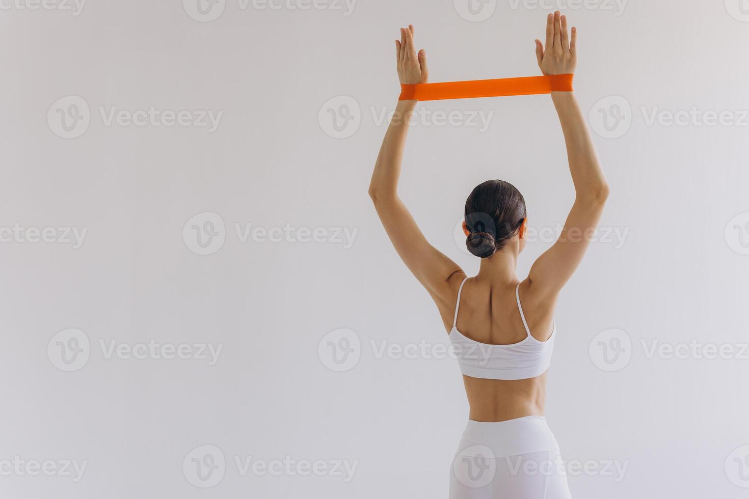Beautiful sports woman with slim body holding resistance band in her hands on white background, back view photo