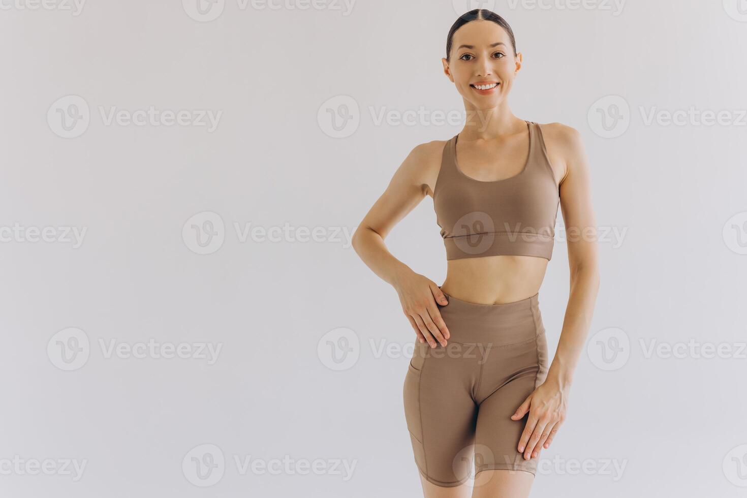 Young slim woman in beige sportwear on white background isolated. Muscular slim attractive female with flat belly. Copy space for text. Body care, healthy and sporty life, hair removal, yoga concept photo