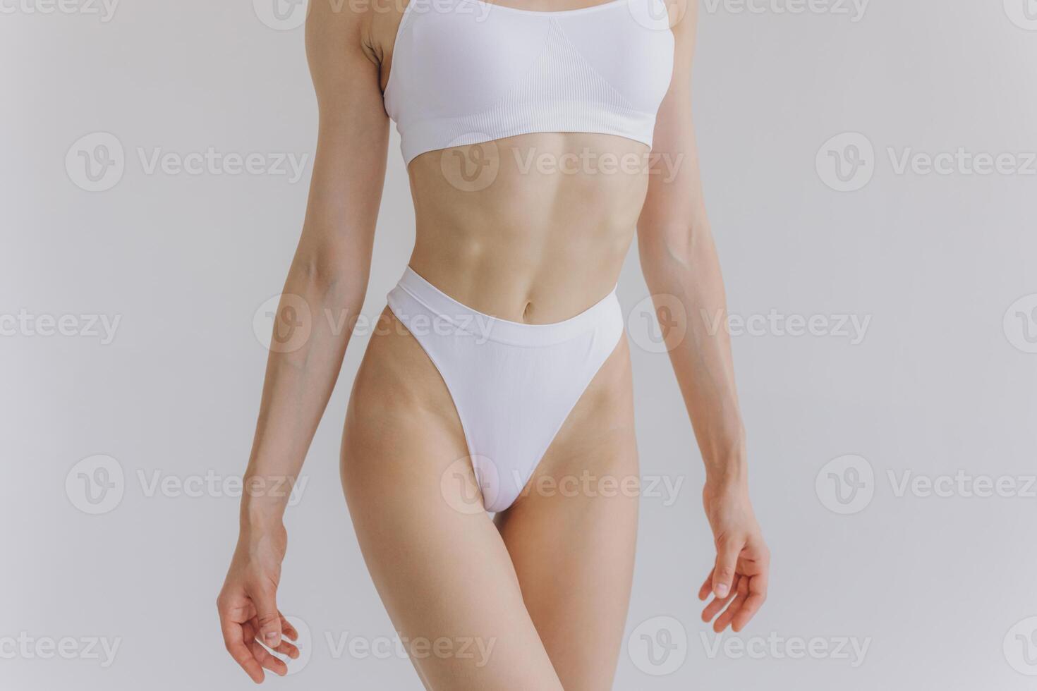 Close up view. Crop image of woman with slim body and perfect stomach in underwear posing in the white studio background. photo