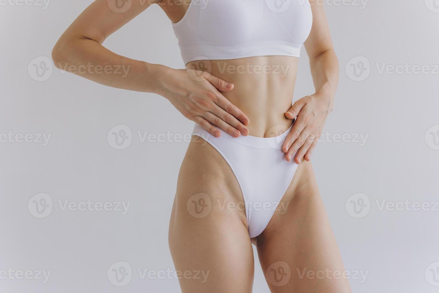 Close up view. Crop image of woman with slim body and perfect stomach in underwear posing in the white studio background. photo