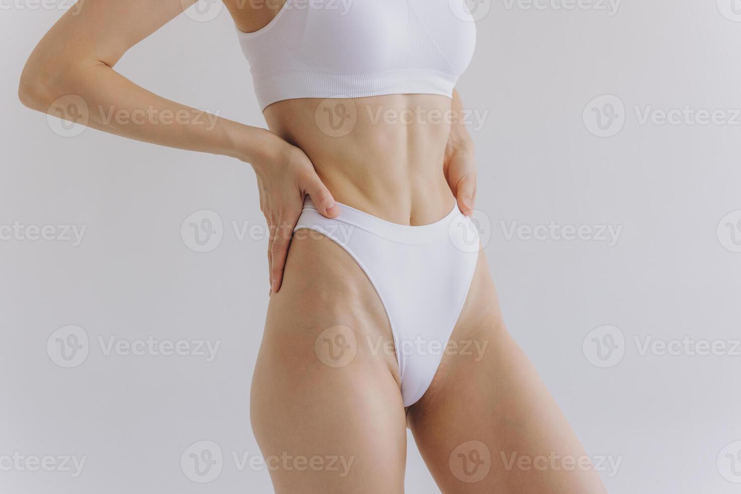 Close up view. Crop image of woman with slim body and perfect stomach in underwear posing in the white studio background. photo