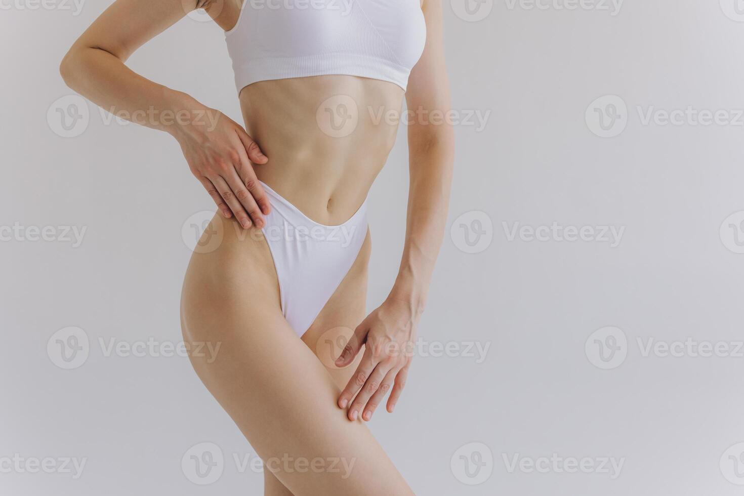 Close up view. Crop image of woman with slim body and perfect stomach in underwear posing in the white studio background. photo