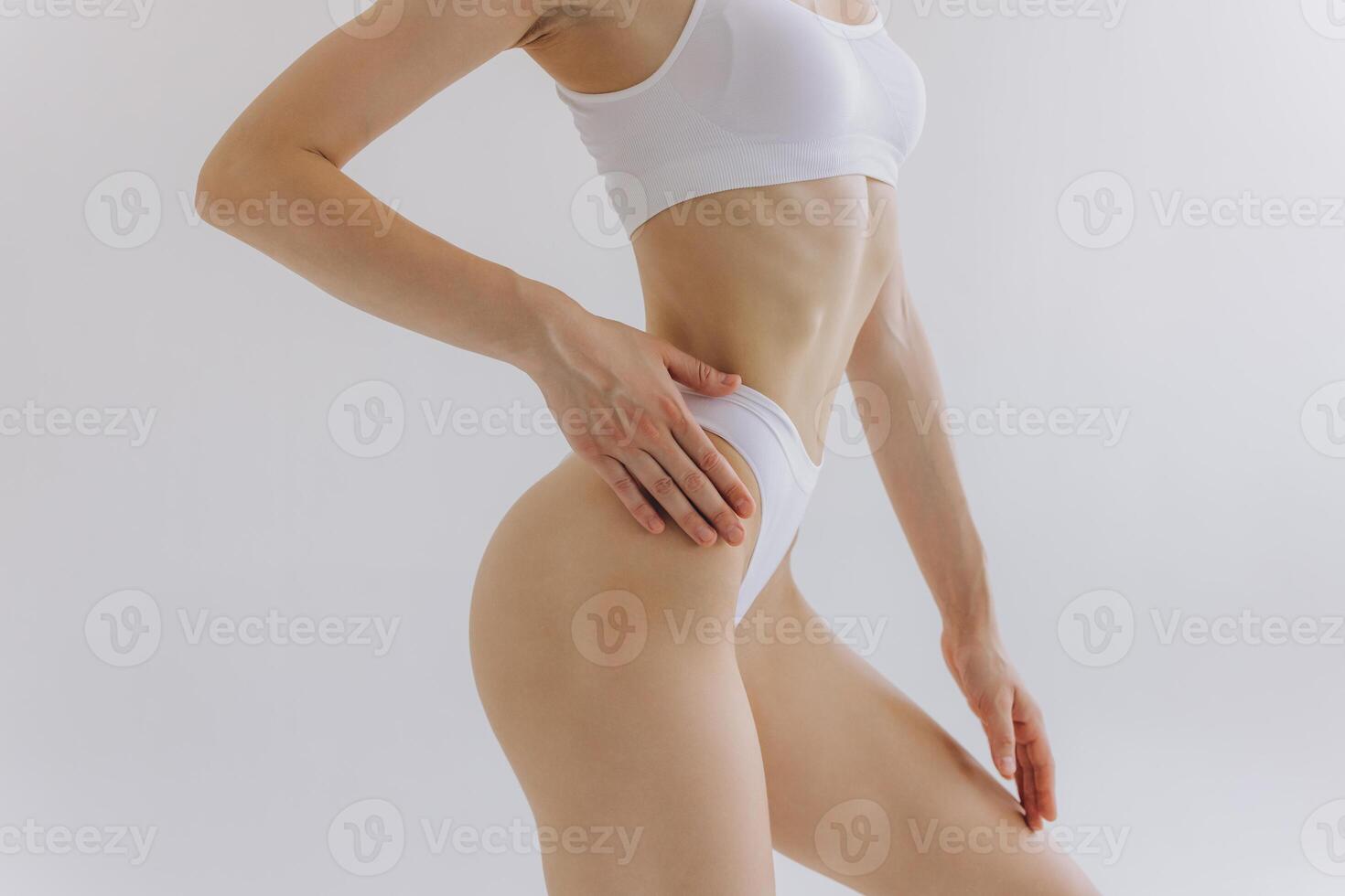 Close up view. Crop image of woman with slim body and perfect stomach in underwear posing in the white studio background. photo