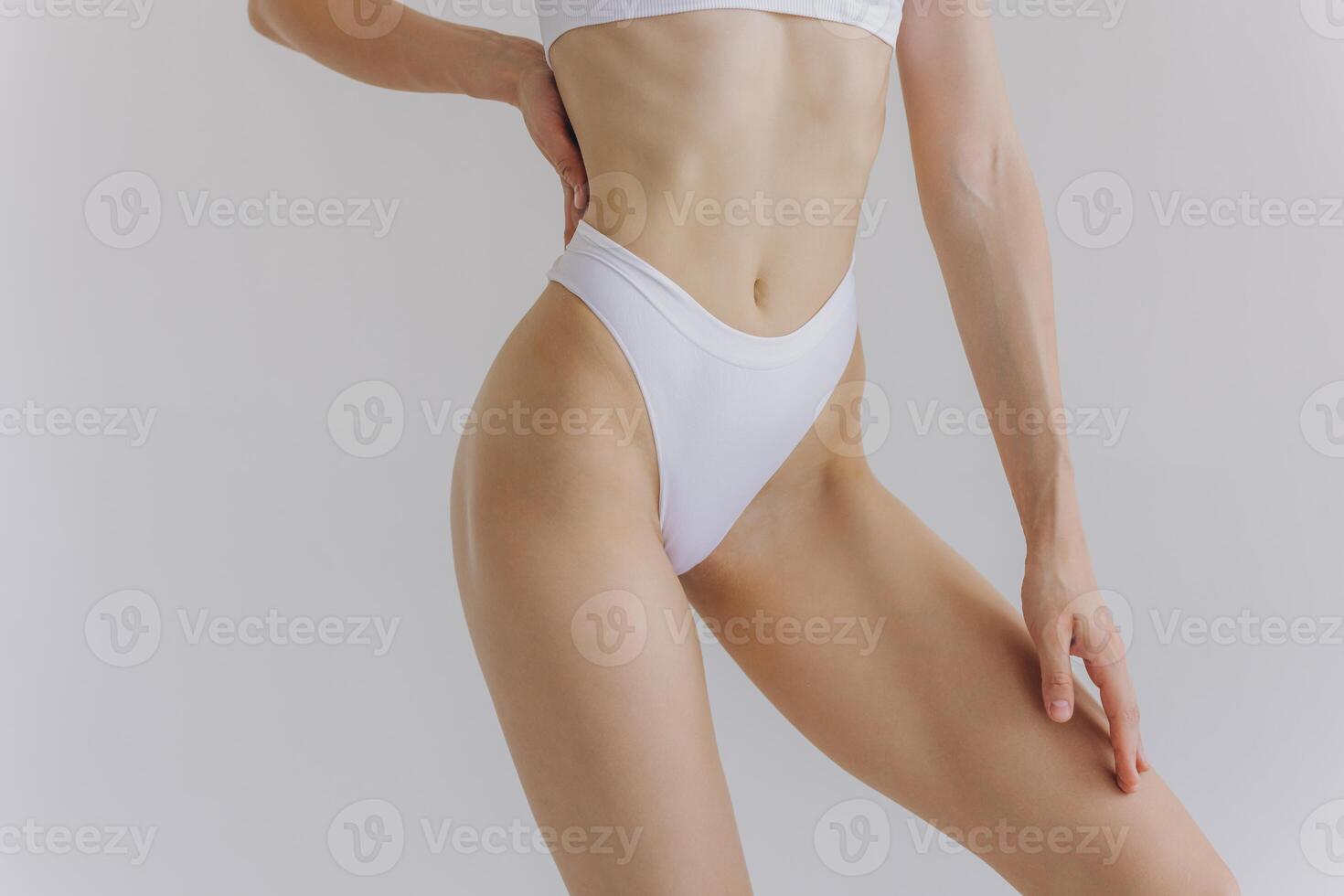 Close up view. Crop image of woman with slim body and perfect stomach in underwear posing in the white studio background. photo