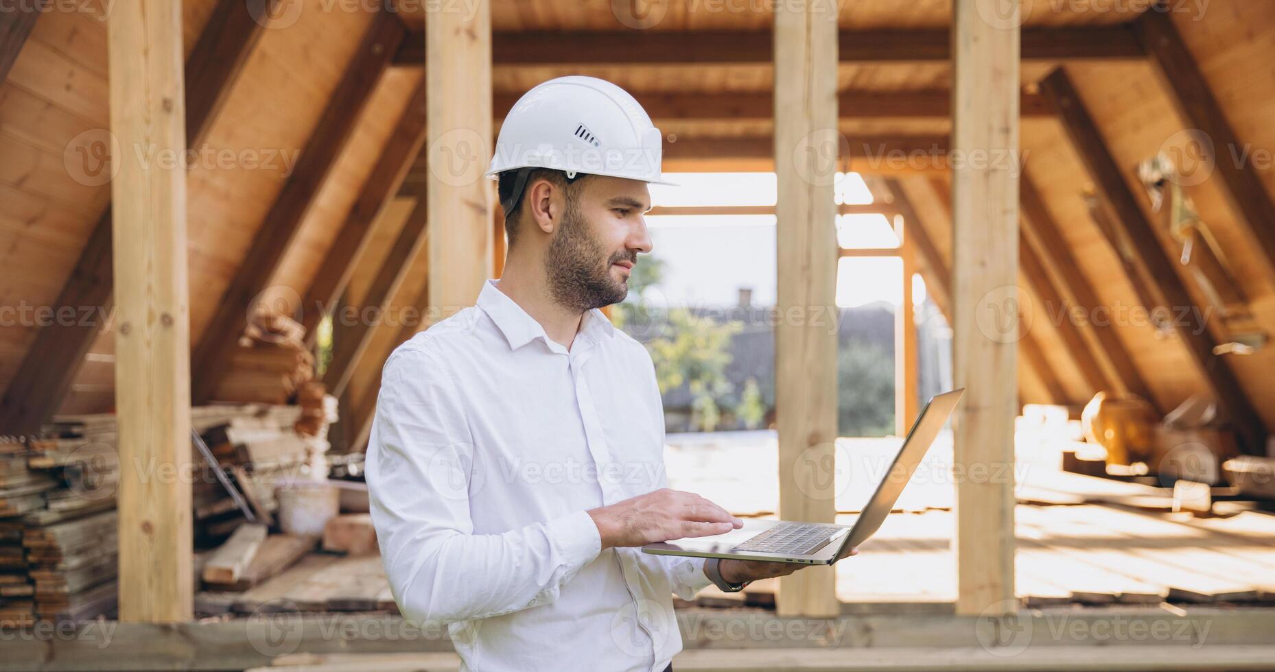 Man builder. Foreman with laptop. Contractor for construction company. Architect in unfinished building. Builder in wooden house under construction. Man engineer from construction team photo
