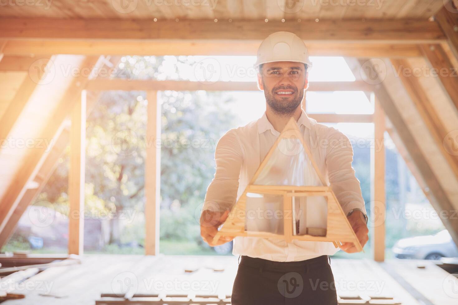 Man builder. Contractor for construction company. Architect in unfinished building. Builder in wooden modular house under construction. Male engineer holding a model of a miniature wooden house photo