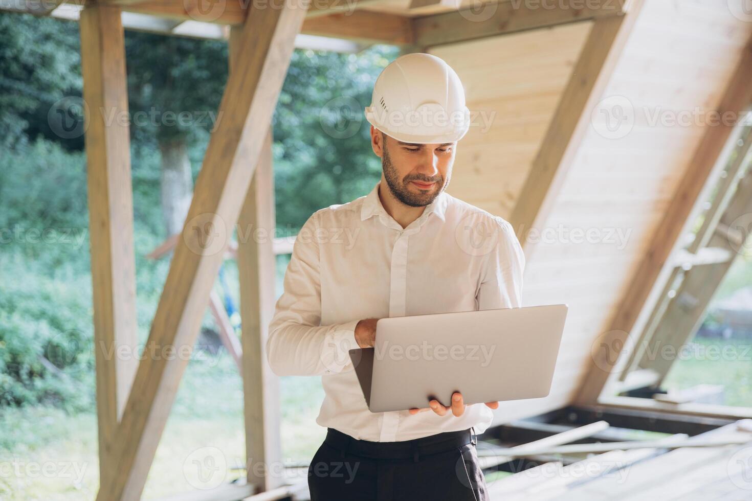 Man builder. Foreman with laptop. Contractor for construction company. Architect in unfinished building. Builder in wooden house under construction. Man engineer from construction team photo