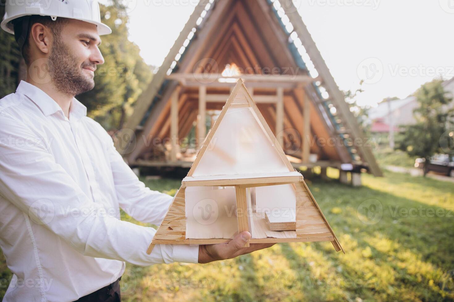 Man builder. Contractor for construction company. Architect in unfinished building. Builder in wooden modular house under construction. Male engineer holding a model of a miniature wooden house photo