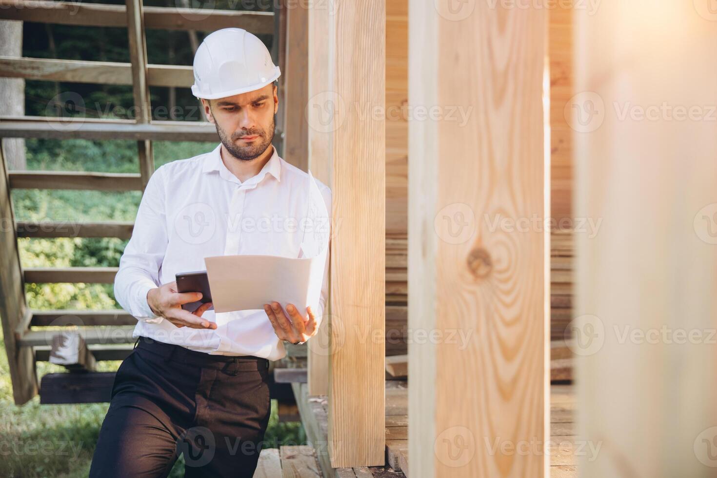 Foreman studies blueprints with tablet. Contractor for construction company. Architect in unfinished building. Builder in wooden house under construction. Man engineer from construction team photo
