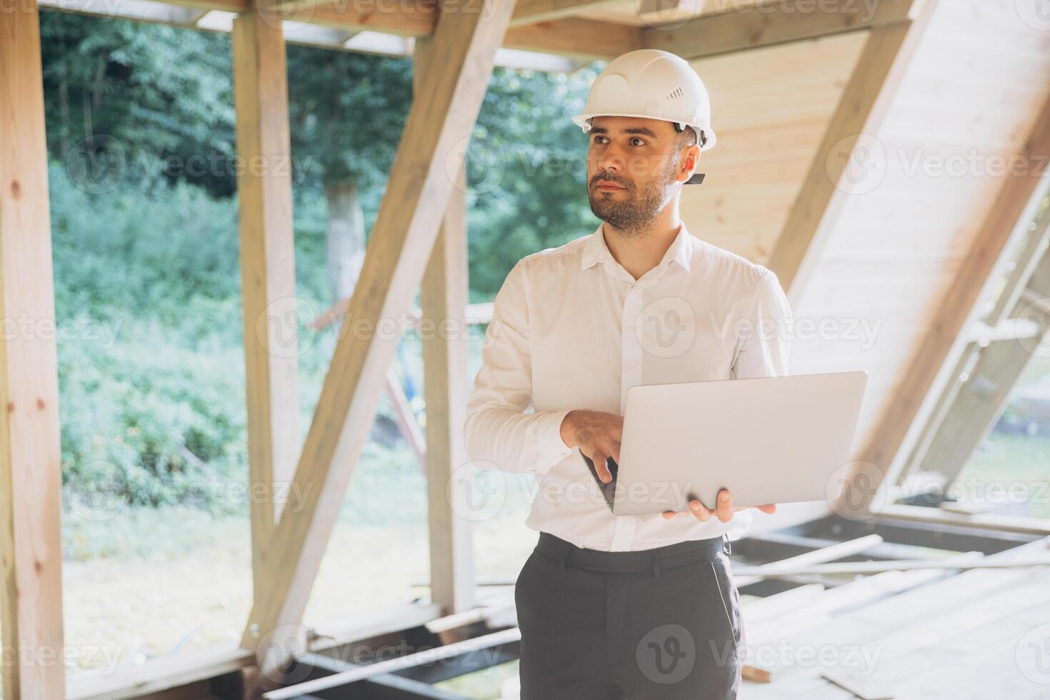Man builder. Foreman with laptop. Contractor for construction company. Architect in unfinished building. Builder in wooden house under construction. Man engineer from construction team photo