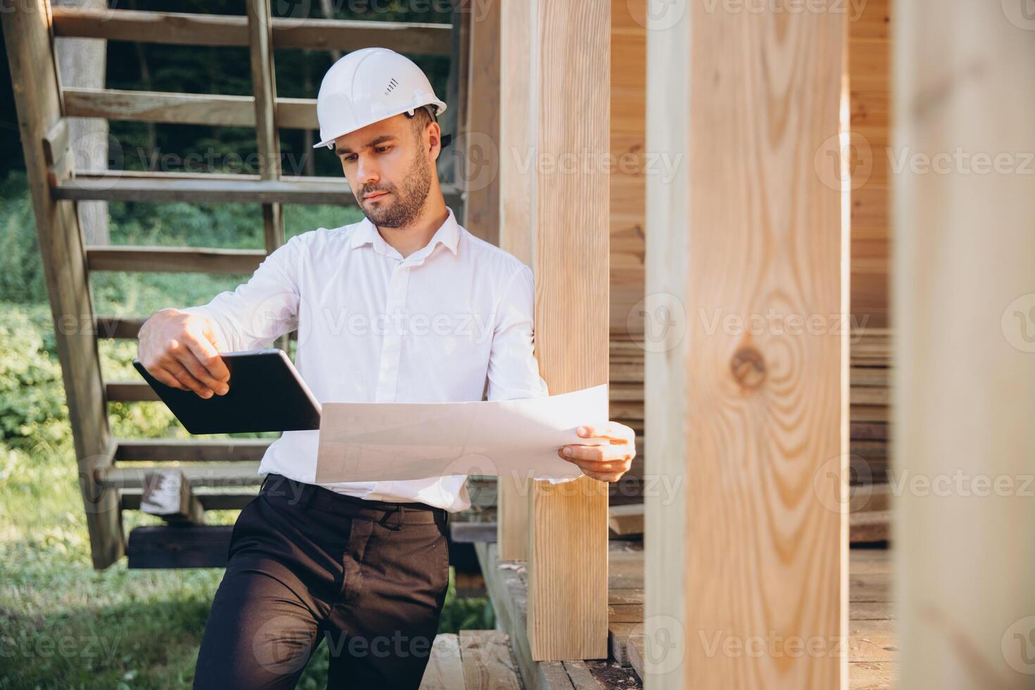 Foreman studies blueprints with tablet. Contractor for construction company. Architect in unfinished building. Builder in wooden house under construction. Man engineer from construction team photo