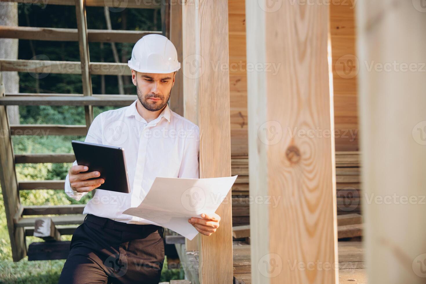 Foreman studies blueprints with tablet. Contractor for construction company. Architect in unfinished building. Builder in wooden house under construction. Man engineer from construction team photo