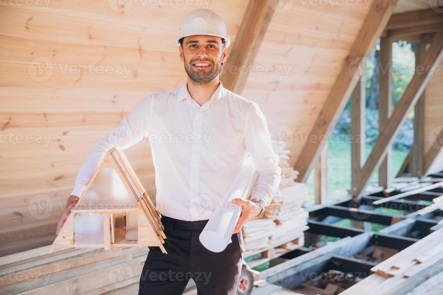 Man builder. Contractor for construction company. Architect in unfinished building. Builder in wooden modular house under construction. Male engineer holding a model of a miniature wooden house photo