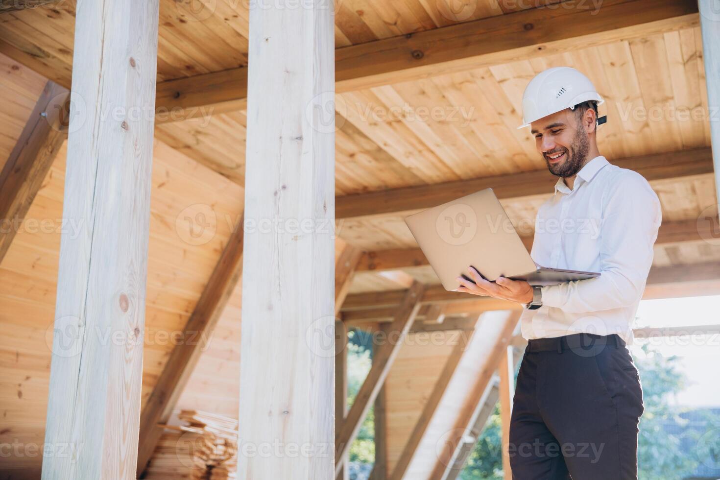 Man builder. Foreman with laptop. Contractor for construction company. Architect in unfinished building. Builder in wooden modular house under construction. Man engineer from construction team photo