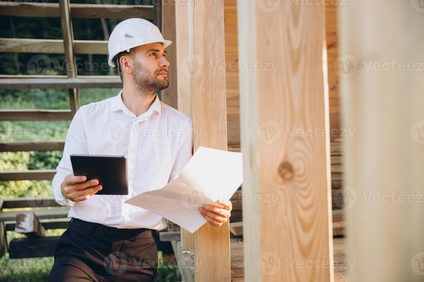 Foreman studies blueprints with tablet. Contractor for construction company. Architect in unfinished building. Builder in wooden house under construction. Man engineer from construction team photo
