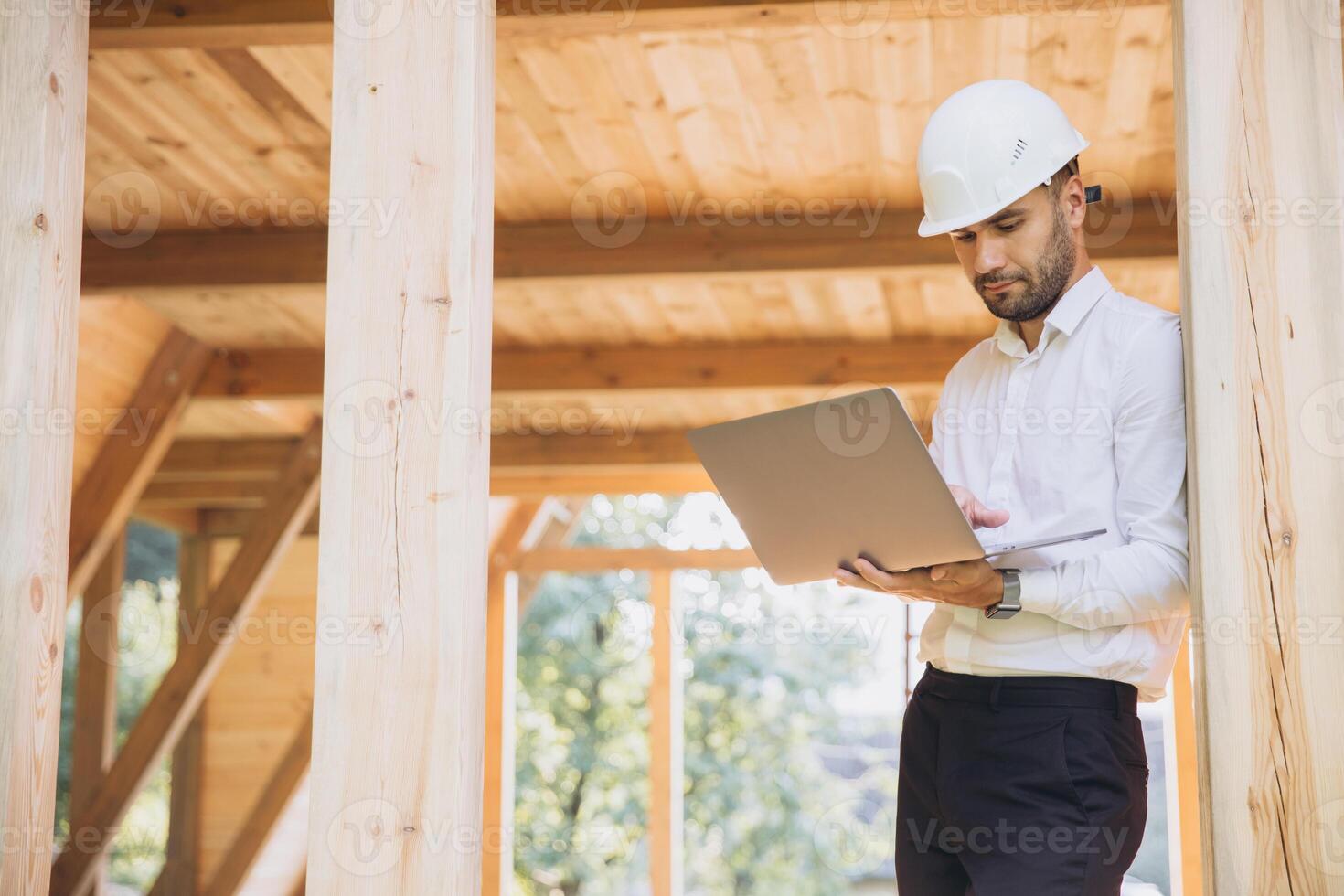 Man builder. Foreman with laptop. Contractor for construction company. Architect in unfinished building. Builder in wooden house under construction. Man engineer from construction team photo