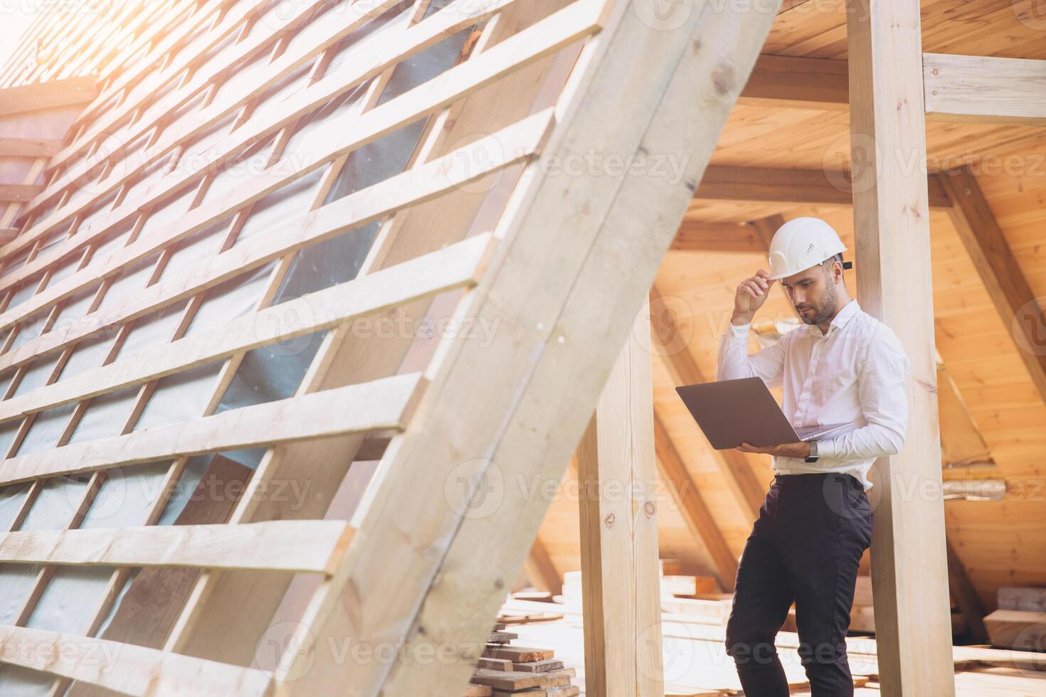 Man builder. Foreman with laptop. Contractor for construction company. Architect in unfinished building. Builder in wooden house under construction. Man engineer from construction team photo