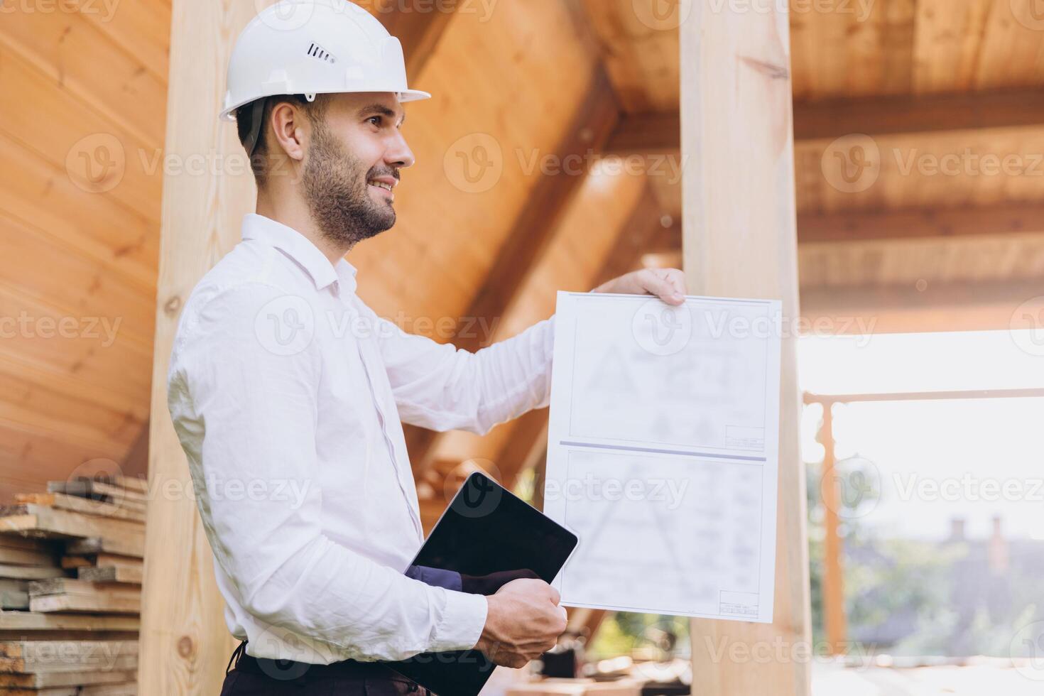 Foreman studies blueprints with tablet. Contractor for construction company. Architect in unfinished building. Builder in wooden house under construction. Man engineer from construction team photo