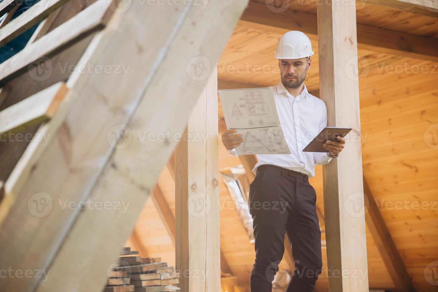 Foreman studies blueprints with tablet. Contractor for construction company. Architect in unfinished building. Builder in wooden house under construction. Man engineer from construction team photo