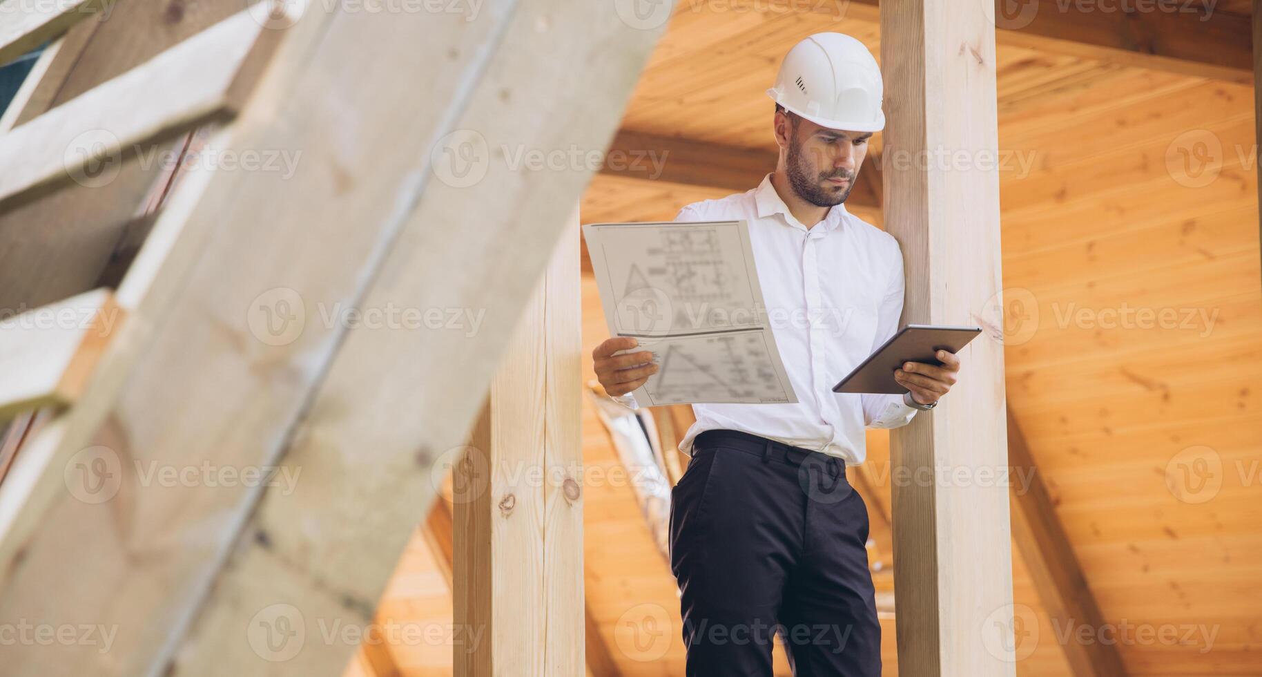 Foreman studies blueprints with tablet. Contractor for construction company. Architect in unfinished building. Builder in wooden house under construction. Man engineer from construction team photo