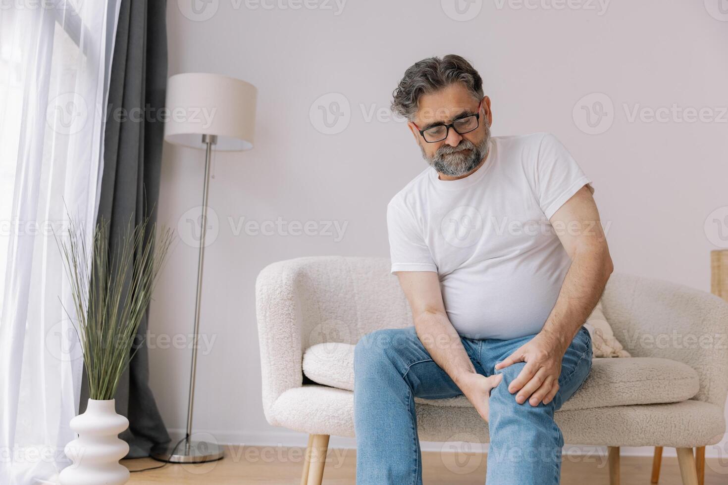 Home, knee pain and senior man with arthritis, osteoporosis and fibromyalgia on sofa. Elderly male with joint massage for relief, muscle tension and accident or injury in retirement photo