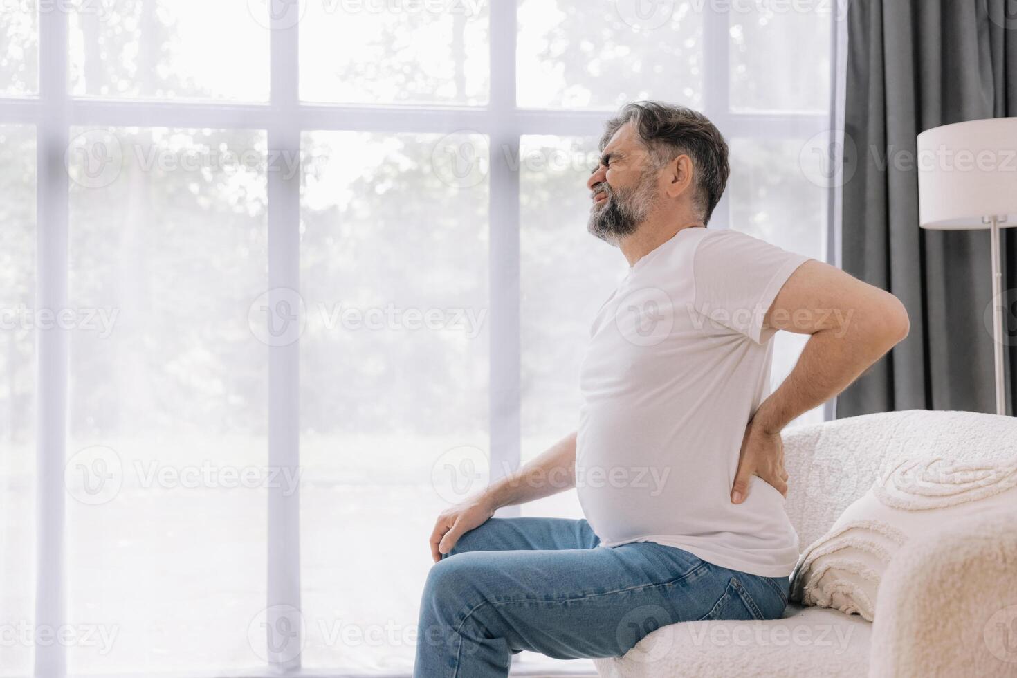 Senior man suffering from back pain on sofa at home photo