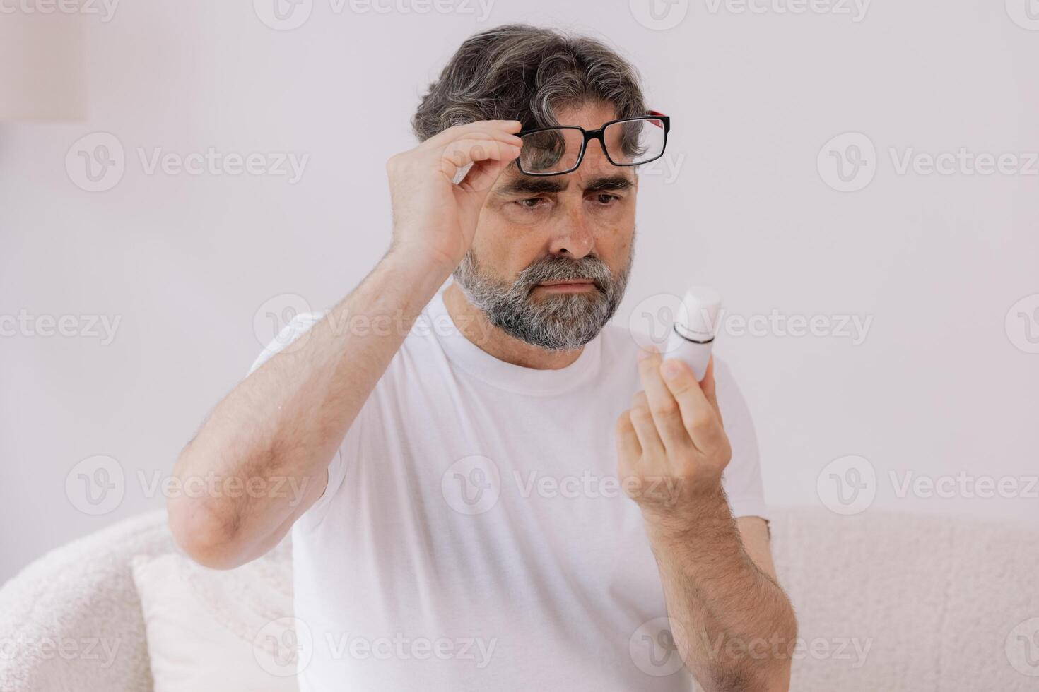 Senior man in glasses with poor vision reads description and instructions for medicine at home, self-care concept, elderly people, copy space, mock up photo