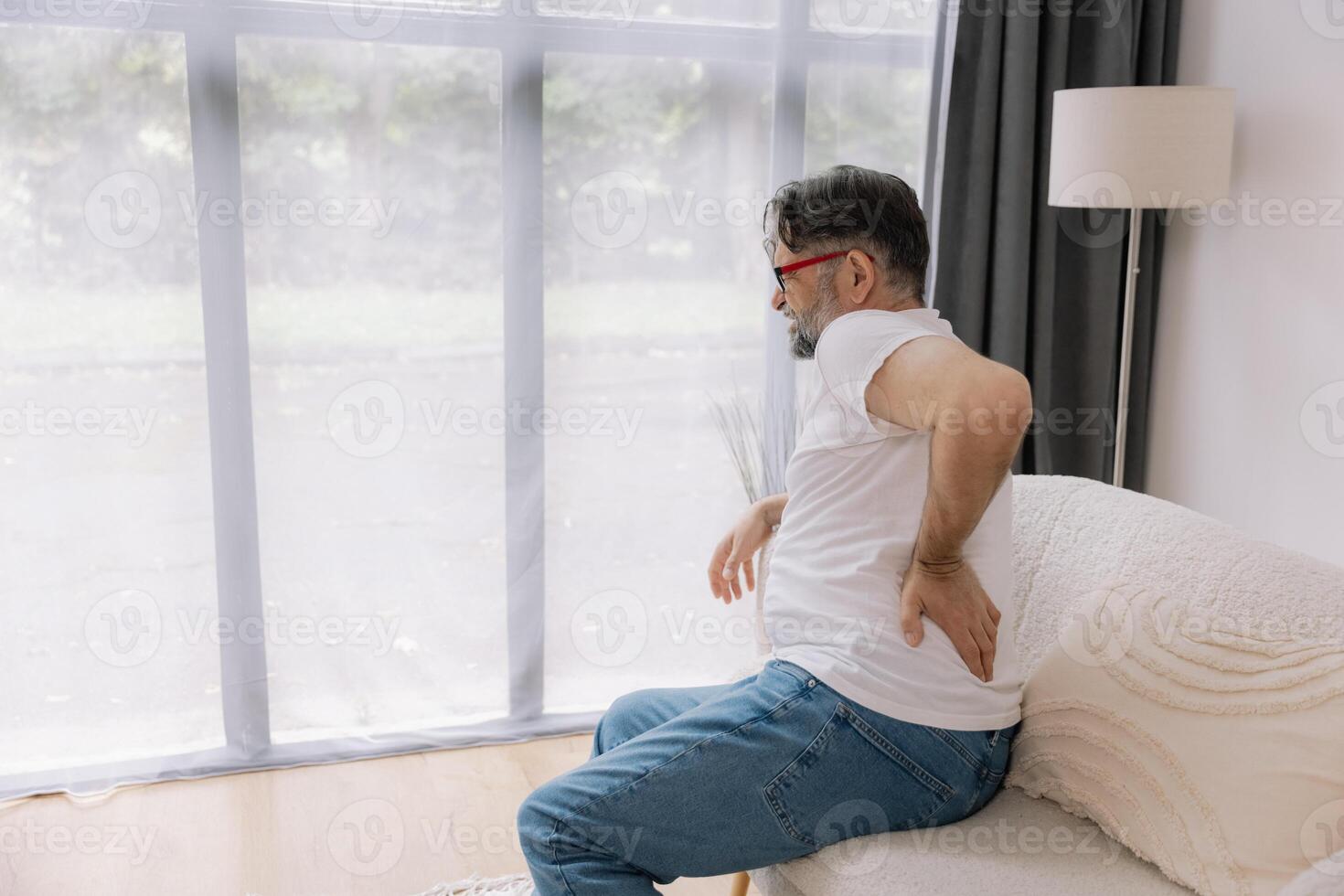 Rear view of Senior man suffering from back pain on sofa at home. photo