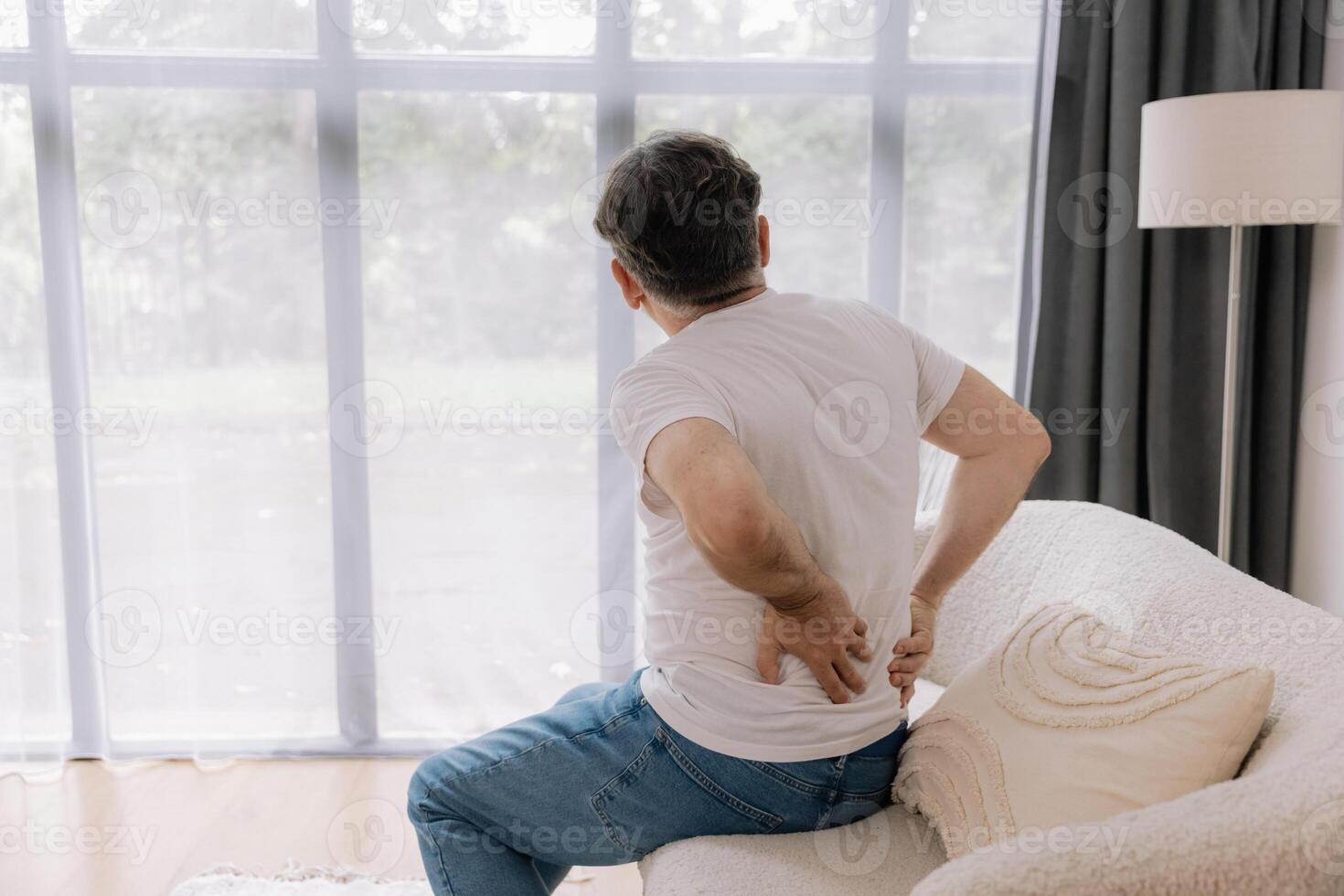 Rear view of Senior man suffering from back pain on sofa at home. photo