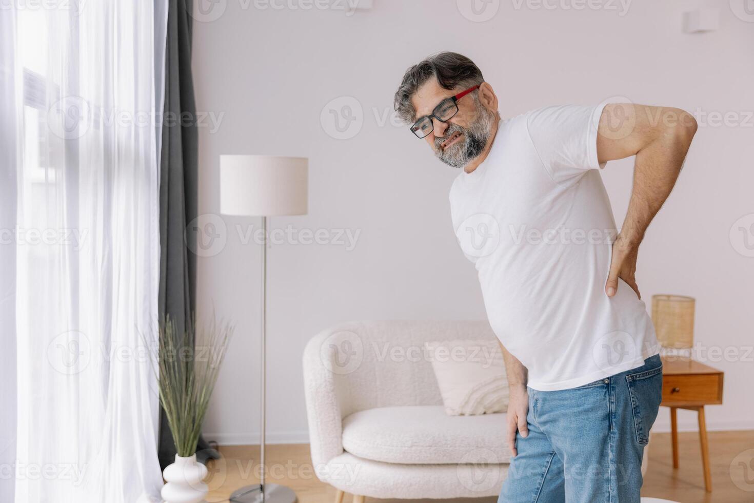 Sick unhappy senior man touching his muscle injury Lower back suffering from muscles back pain at home. Physical injury and healthcare problem photo