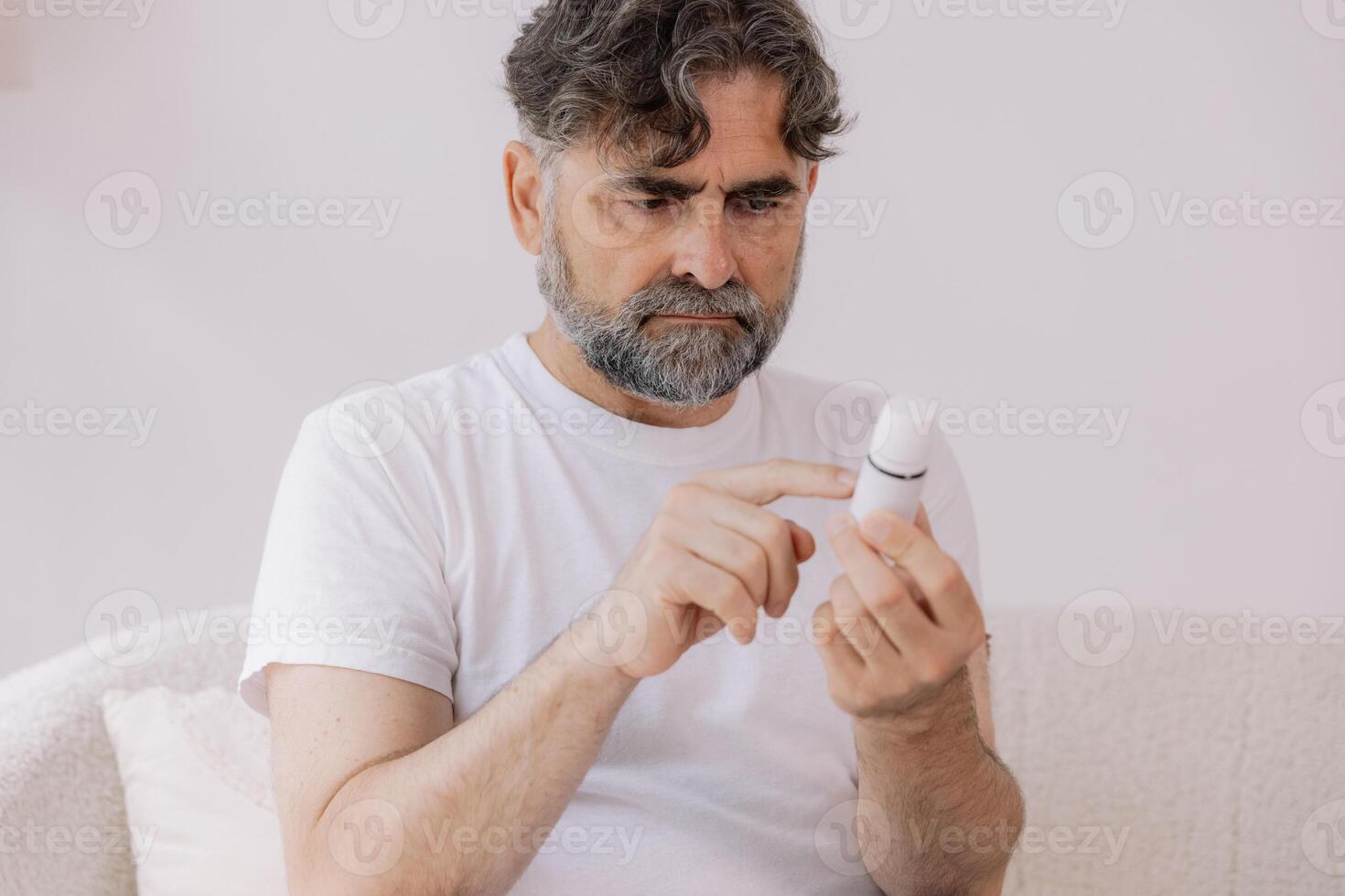 Senior man in glasses with poor vision reads description and instructions for medicine at home, self-care concept, elderly people, copy space, mock up photo