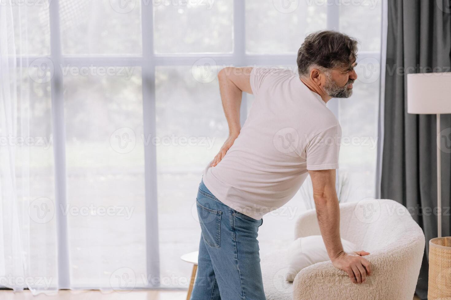 Rear view of senior man suffering from back pain on sofa at home, copy space for your advertising photo