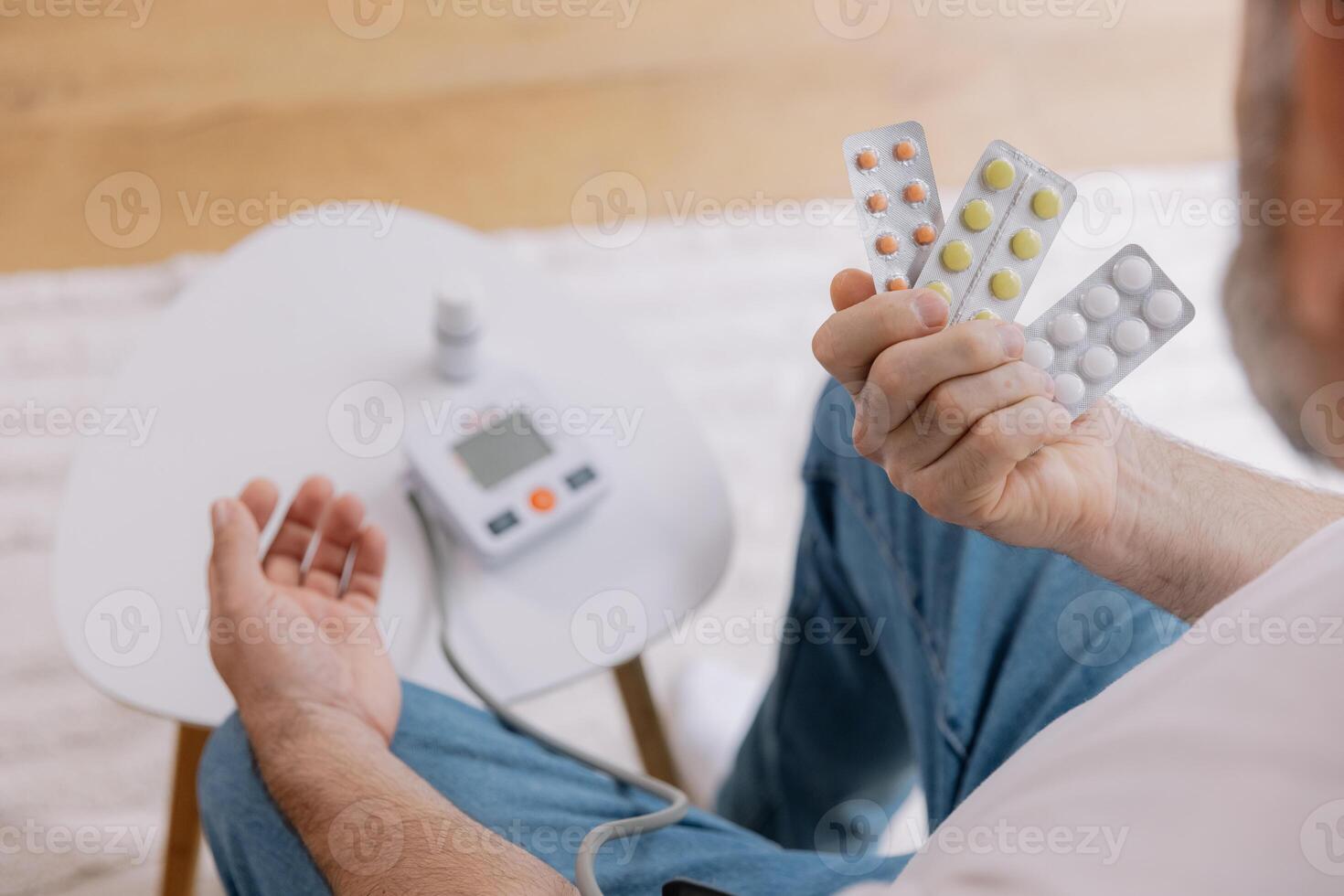 Close-up of elderly man sitting sofa at living room measures blood pressure with device. Senior male holding pills and drops drugs. Health and self-care concept, copy space photo