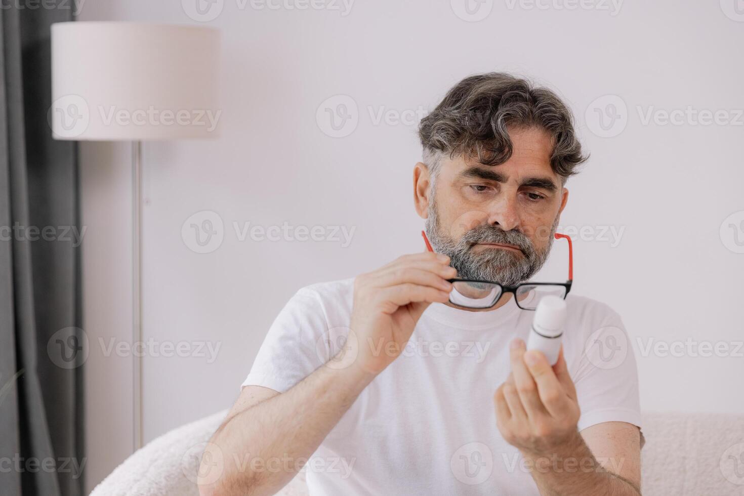 Senior man in glasses with poor vision reads description and instructions for medicine at home, self-care concept, elderly people, copy space, mock up photo