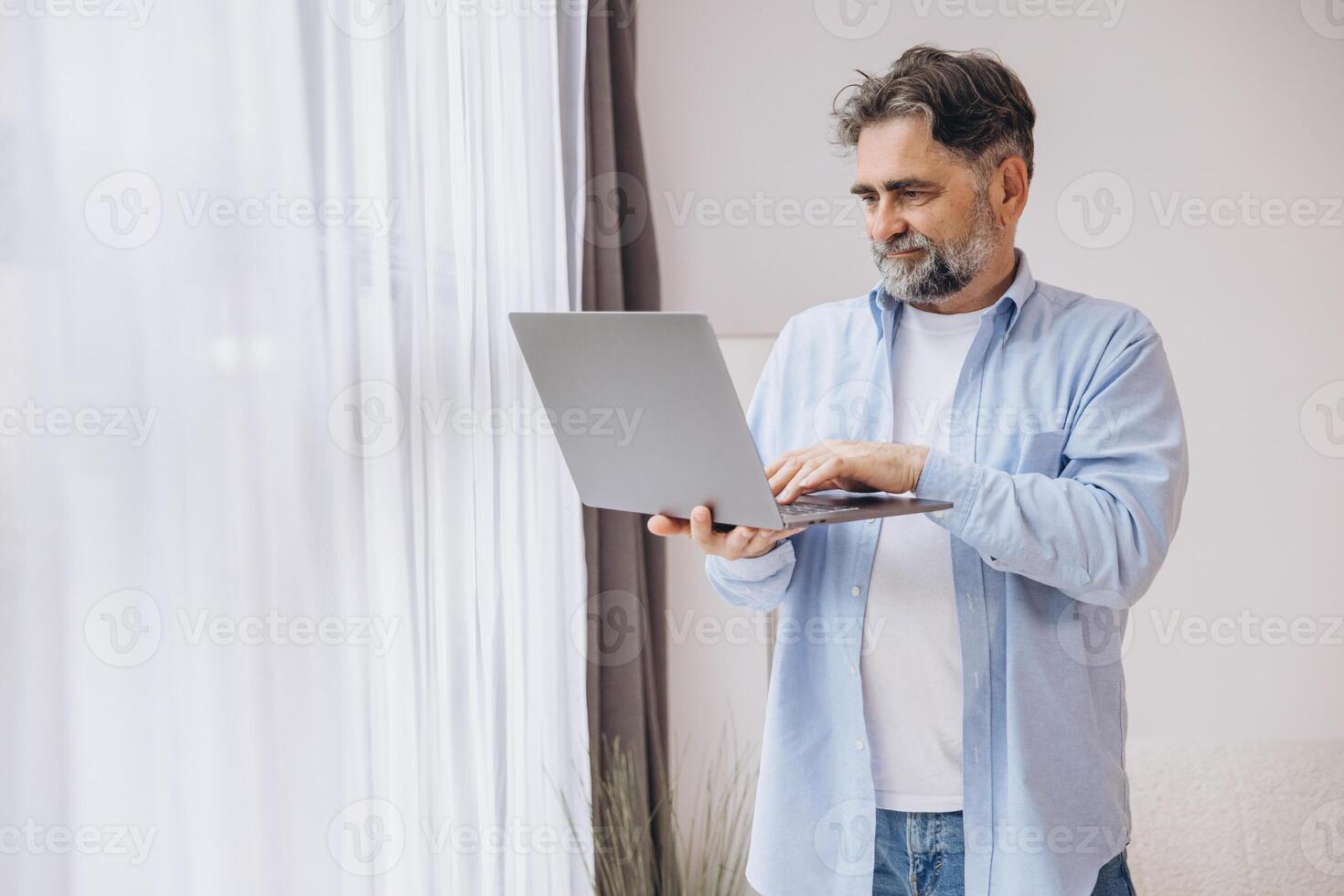 Smiling mature man using laptop in living room. Happy confident senior male adult resting at home working on pc, typing on keyboard, copy space photo