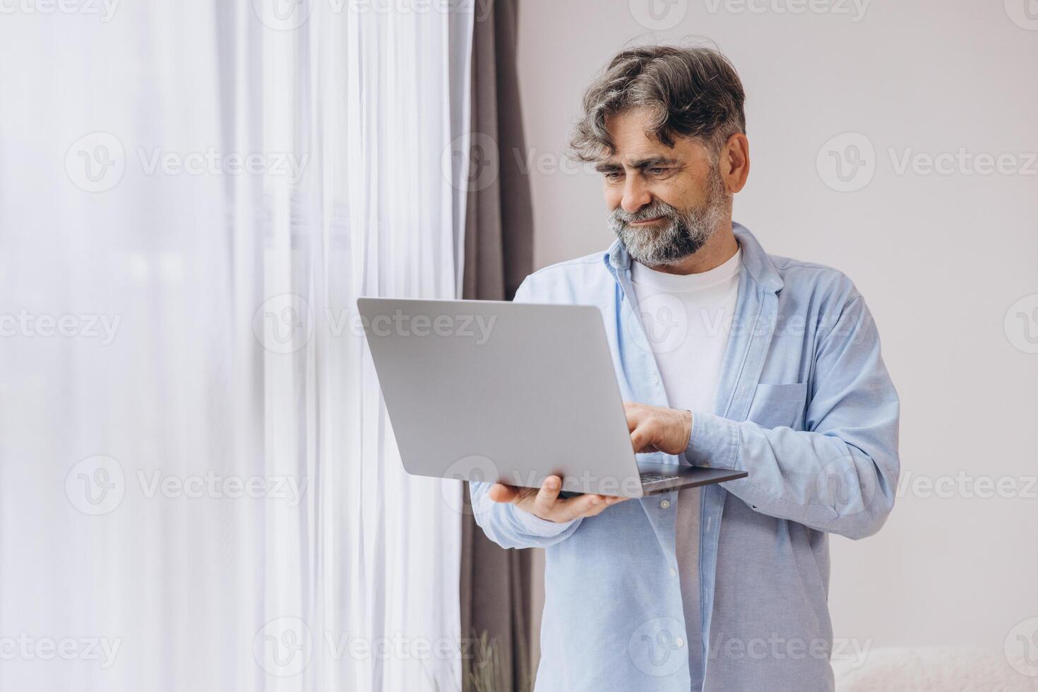 Smiling mature man using laptop in living room. Happy confident senior male adult resting at home working on pc, typing on keyboard, copy space photo