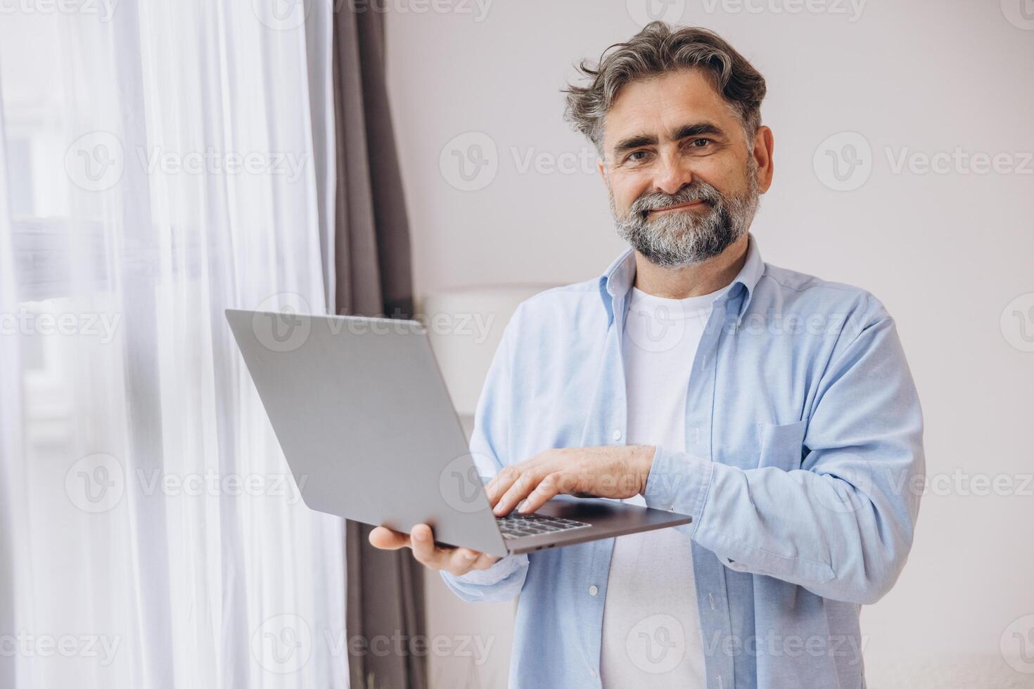 Smiling mature man using laptop in living room. Happy confident senior male adult resting at home working on pc, typing on keyboard, copy space photo