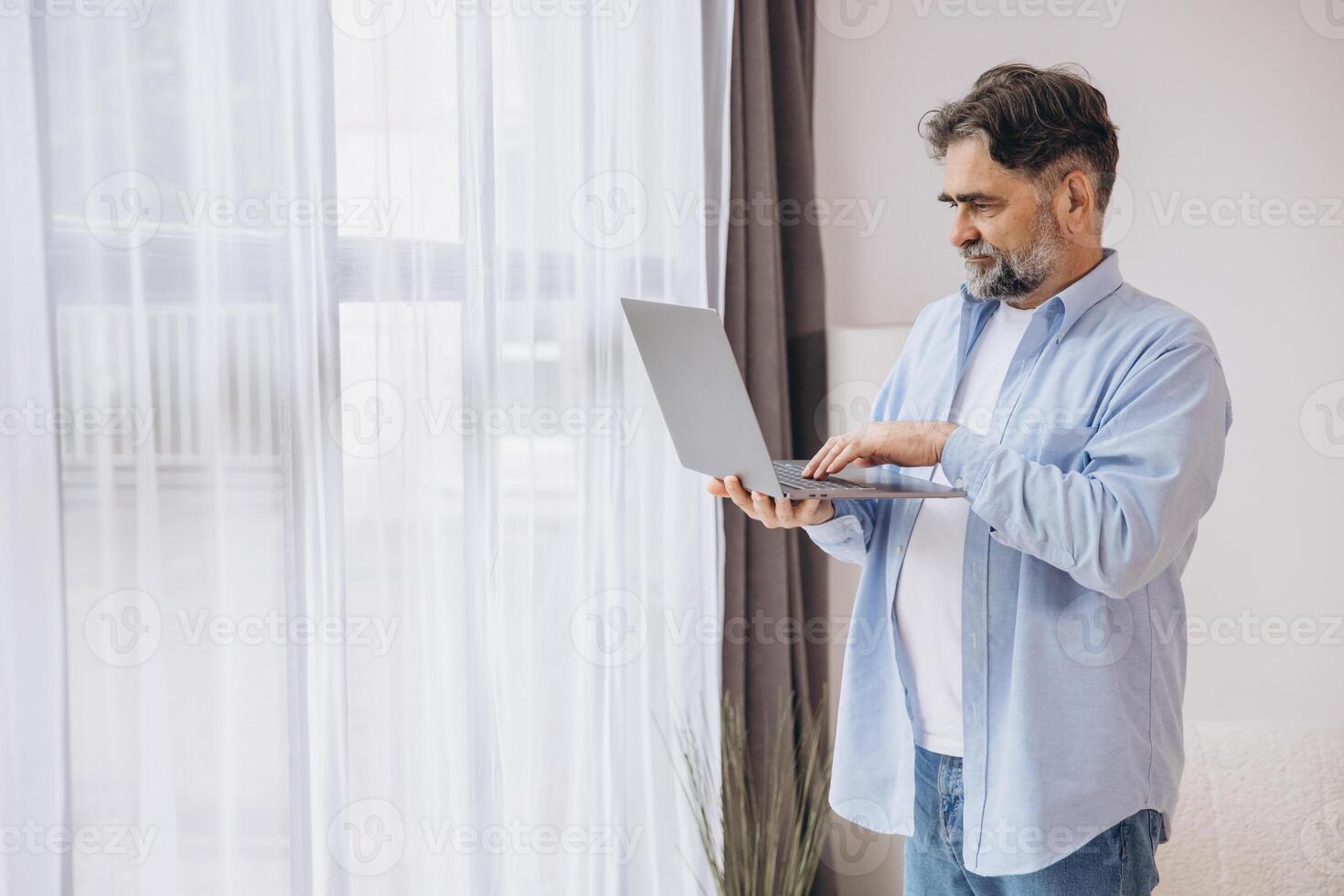 Smiling mature man using laptop in living room. Happy confident senior male adult resting at home working on pc, typing on keyboard, copy space photo