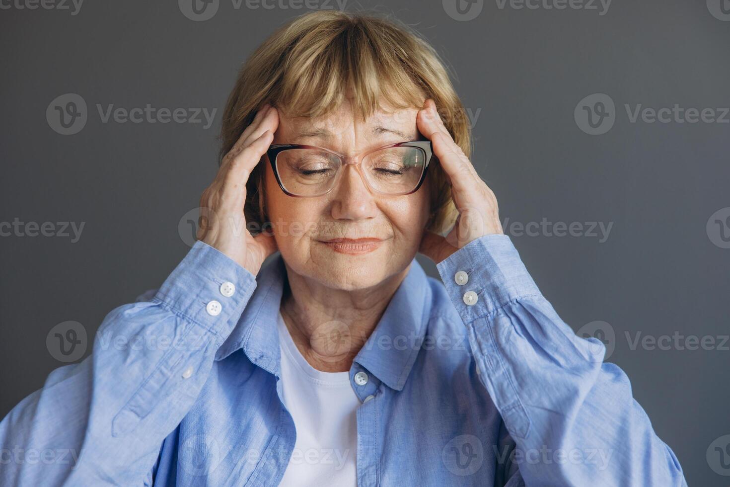 Portrait of senior woman at home with a headache, feeling pain and with an expression of being unwell on gray background photo